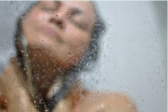 Woman washing hair as seen through a glass shower stall.