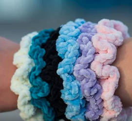 A hand with hair scrunchies in blues, black, white, purple and pink.